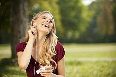 Frau sitzt im Park und hört Musik mit einem MP3 Player