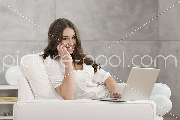 junge Frau mit Laptop sitzt auf Sofa und Telefoniert 