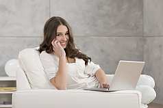 junge Frau mit Laptop sitzt auf Sofa und Telefoniert 