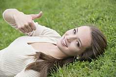 junge Frau liegt im Gras und gibt Handzeichen