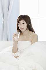 Junge asiatische Frau sitzt im Bett mit einem Glas Wasser in der Hand