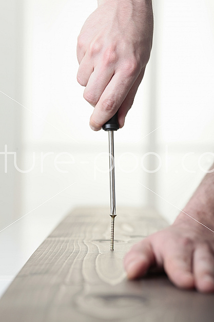 Männerhände drehen Schraube in Holz