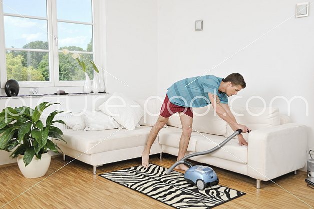 junger Mann saugt sein Sofa 