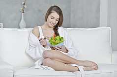 junge Frau sitzt auf dem Sofa und isst Salat 