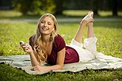 junge Frau liegt im Park und hört Musik mit einem MP3 Player