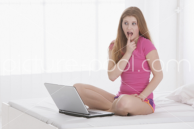 junge Frau sitzt mit Laptop auf dem Bett