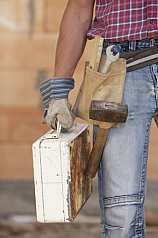 Männlicher Bauarbeiter mit Werkzeug und Metallkoffer vor Ziegelsteinmauer