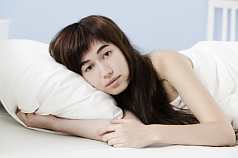 Junge asiatische Frau im Bett zugedeckt